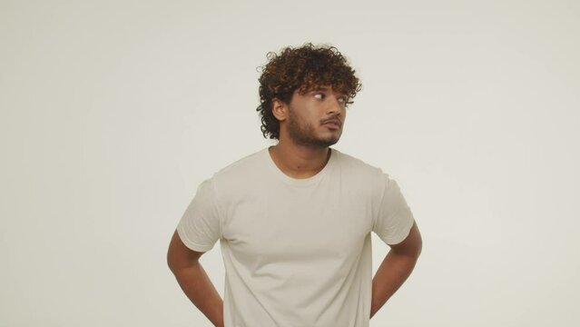 Curly Indian guy is dancing isolated on white background. Handsome young man in t-shirt enjoying music rhythm and making dance moves