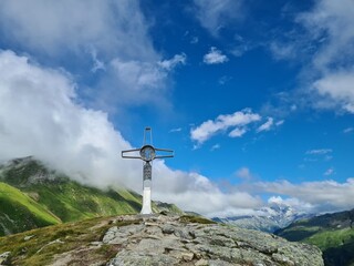 A metal summit cross of the top of Bockhartscharte in Austrian Alps. Hohe Tauern. Clear and sunny day. Outdoor activity. Barren top of the mountains