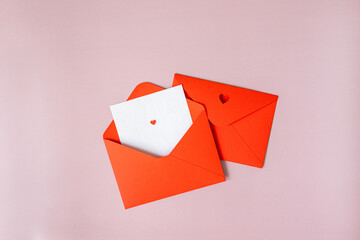 two red envelopes on a pink background lie in the center, one is open, a white sheet of paper sticks out of it, a letter with a heart, the other letter is closed