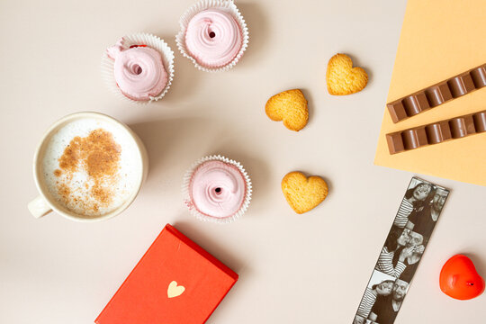 the mood of valentine's day, on a beige background there is a mug of cappuccino, a red box with a gift, candles, photos of a couple from a photo booth, heart-shaped cookies, pink marshmallows