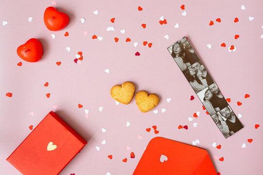 the mood of valentine's day, on a pink background in the center are two heart-shaped cookies, a red box with a gift, an envelope, candles, photos of a couple from a photo booth