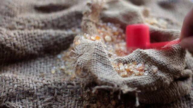 Close-up shot of gond,goond,edible gum, or gund katira crystals in a wicker basket on gunny bag surface along with its oil in a transparent bowl.