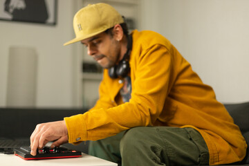 Biracial man making beats from his sofa at the coffee table with an MPD MIDI controller - Powered by Adobe