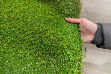 Buying an artificial grass mat. Woman choosing a bright green artificial grass rug in a store
