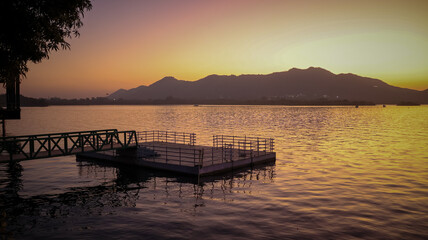 Fototapeta na wymiar Udaipur, Rajasthan, India 21st January 2023: Beautiful Sunset view from a park around Lake Pichola in Udaipur City. Romantic sunsets in udaipur Doodh Talaki Lake, Lake Pichola, Monsoon.