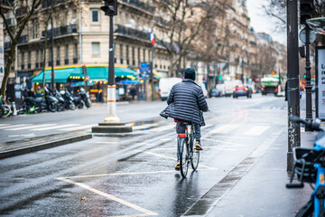 Active Lifestyle in Paris: Man Cycling on a Rainy Day through the Charming Old City Streets with Wet Pavement, Wearing a Jacket from the Back