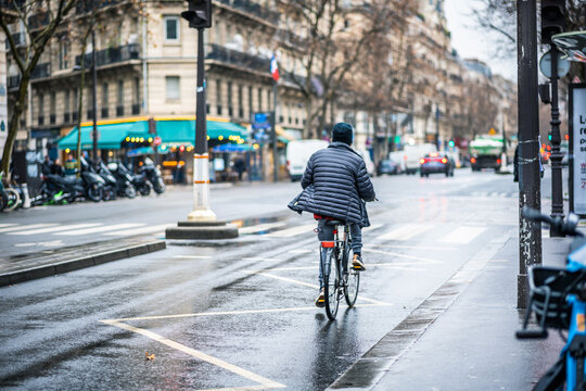 Active Lifestyle in Paris: Man Cycling on a Rainy Day through the Charming Old City Streets with Wet Pavement, Wearing a Jacket from the Back - Powered by Adobe
