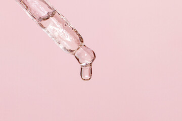 Cosmetic pipette with dripping liquid and drops on a pink background, serum, serum, gel, vitamin, water, oil