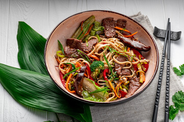 Udon stir fry noodles with beef meat and vegetables in a plate on white wooden background.
