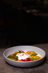 Salad with buratta cheese and tomatoes with pesto sauce in a bowl on a black background