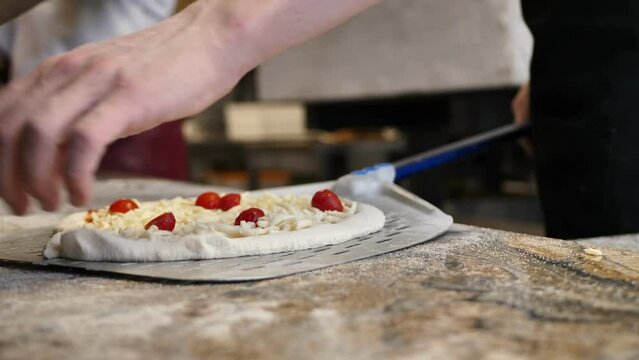The cook in the kitchen puts pizza on a shovel before baking in a wood-burning oven.