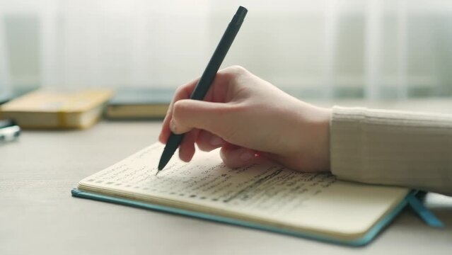 close-up of a female hands taking notes in a notebook notepad using pen on modern desk at home young woman writes in a diary with a pen while sitting at the table Close up commonplace