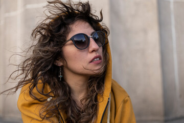 Latina woman, windblown curly hair, hoodie, sunglasses, with relaxed and thoughtful attitude