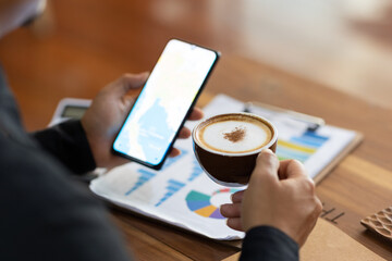 Young Asian man in black long-sleeved shirt sitting working in a cafe Use your smartphone and documents on the table.