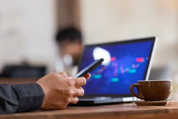 Close-up shot of young asian man using smartphone and laptop working in cafe.
