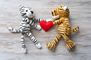 a yellow tiger and a white tiger hold a heart with their paws on a gray background