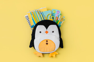 Plush penguin backpack with stationery and supplies for drawing and craft on yellow background....