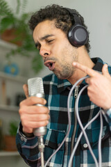 Mixed race man dressed in checked shirt singing into a condenser microphone