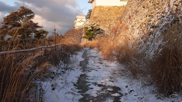 Slow tilt up from snow covered path to Japanese castle in morning golden light