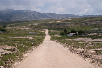 Fototapeta premium View of the dirt road across the green field and rocky hills.