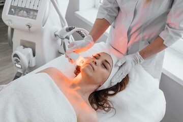 Red LED treatment. Woman doing facial skin therapy. Radiofrequency face lifting. Hardware antiaging...