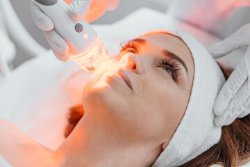 Red LED treatment. Woman doing facial skin therapy. Radiofrequency face lifting. Hardware antiaging...