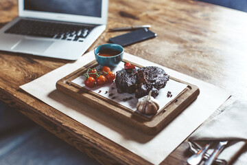 Grilled ribeye beef steak, herbs and spices and tomato cherry with laptop on the background. High quality photo