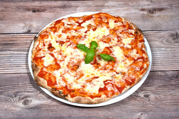 Pizza margherita with tomato mozzarella and basil in a plate isolated on wooden background