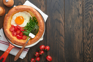 Dutch baby pancake. Fresh homemade Dutch Baby pancake with fried egg, tomato and green arugula in reed cast-iron pan on old wooden table. Flat lay, close up.