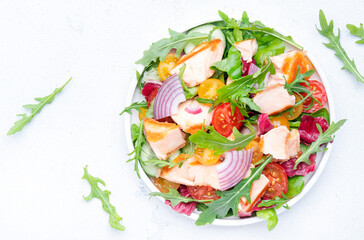 Grilled salmon fish salad with tomato, cucumber, arugula, radicchio, red onion and lettuce with lemon and sesame seeds. Healthy eating delicious lunch. White table background, top view