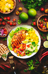 Grilled chicken salad with avocado, mango, tomato salsa, cilantro and lettuce in mexican style, rustic wooden table background, top view