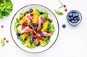 Gourmet salad with smoked duck, oranges, blueberries, cranberries, arugula and lettuce, white table background, top view