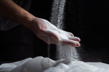 Sand through fingers on black background. Concept of the flow of life.