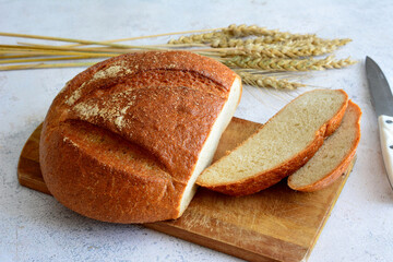 fresh round bread with slices on cutting board and kitchen knife and ears of wheat, close-up