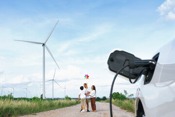 Concept of progressive happy family holding windmill toy and relax at wind farm with electric...