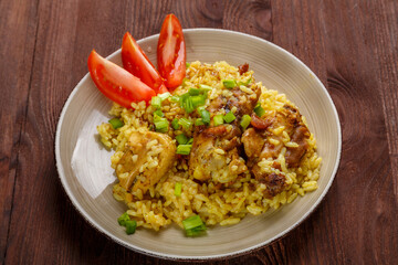 Rice chicken in teriyaki sauce garnished with green onions on a wooden table.