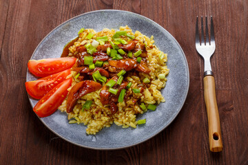 Rice chicken in teriyaki sauce garnished with green onions on a wooden table next to soy sauce next to a fork.