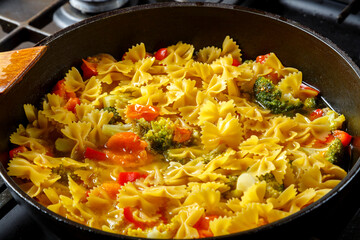 Farfalle pasta with stewed fresh vegetables and spices in a frying pan.