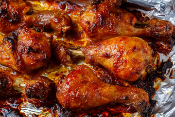 Chicken legs baked in sauce and spices on foil close-up.