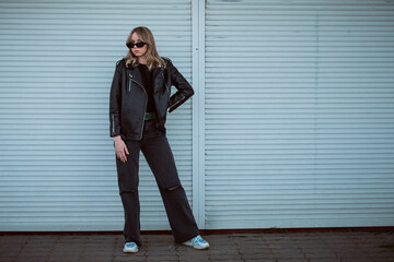 Obraz premium beautiful girl model with coffee in a black jacket in a black baseball cap on a chair sitting outside on the stairs posing for the camera with a phone in green clothes in sneakers fashion
