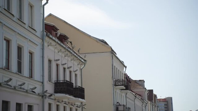 Old restored building of different heights in city with tiled roof, drainpipe, attic and balconies. Along edge of gable triangular roofs are decorative lighting lanterns. 
