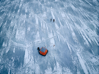 Two friends, fishing on ice in the north Arctic in an orange tent.