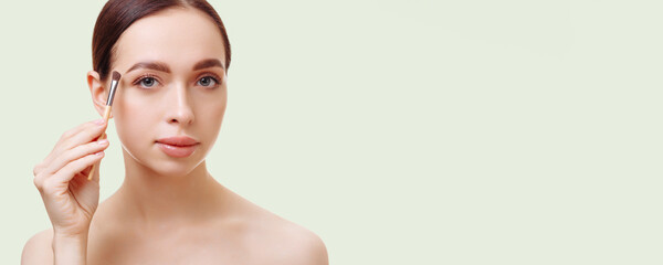 Banner portrait of an attractive young brunette woman plucking her eyebrows against a white background. Holds tweezers in hand. The concept of eyebrow care, cosmetic procedures.