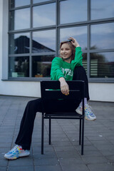 Obraz na płótnie Canvas beautiful girl model with coffee in a black jacket in a black baseball cap on a chair sitting outside on the stairs posing for the camera with a phone in green clothes in sneakers fashion