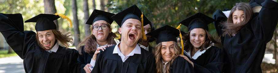 A group of graduates in robes congratulate each other on their graduation outdoors. Widescreen. 