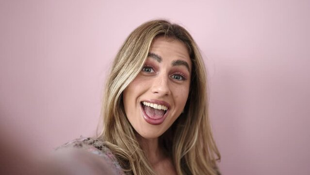 Young blonde woman smiling confident making selfie by camera over isolated pink background