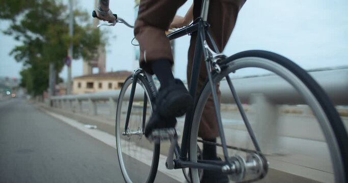 Close up on rear wheel of commuter bicycle. Young man pedaling on simple single speed bike on way to work. Student ride his bike on way to school or university. Commuting in big city