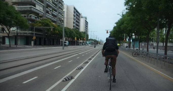 Follow shot of young man ride bike in city, on bike lane. Urban city planning infrastructure for cyclists. Speeding up to arrive in time. Eco friendly and efficient transportation choice