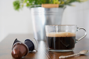 Cup of black coffee next to some capsules