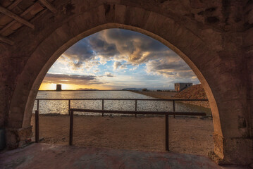 Sunset at the Trapani salt pans seen from a stone arch, Sicily
